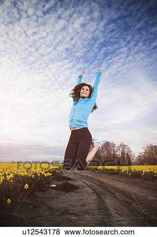 Stock Photo - USA, Washington, Skagit Valley, Woman in blue tracksuit jumping in air. Fotosearch
