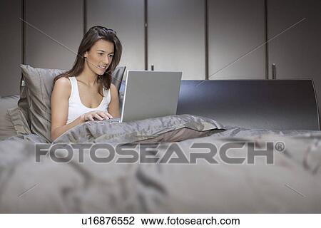 Stock Image - Woman in bed using laptop. Fotosearch