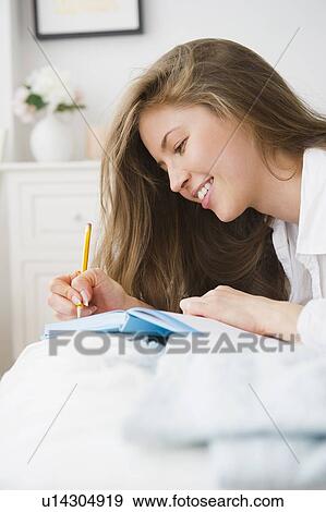 Stock Photo - Woman lying on bed and writing diary. Fotosearch