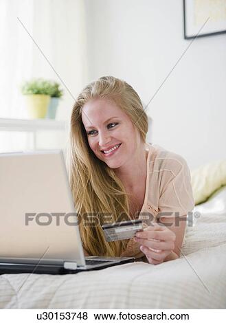 Woman online shopping while lying on bed View Large Photo Image Stock Photo - Woman online shopping while lying on bed. Fotosearch