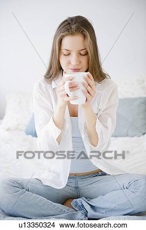 Picture - Woman sitting on bed drinking coffee. Fotosearch