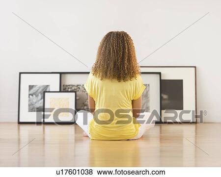 Stock Photo - Woman sitting on floor looking at artworks. Fotosearch