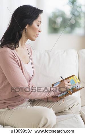 Woman sitting on sofa and writing in personal organizer View Large Photo Image Stock Photo - Woman sitting on sofa and writing in personal organizer. Fotosearch