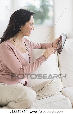 Woman sitting on sofa using digital tablet View Large Photo Image Picture - Woman sitting on sofa using digital tablet. Fotosearch