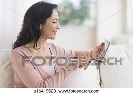Woman sitting on sofa using digital tablet View Large Photo Image Stock Image - Woman sitting on sofa using digital tablet. Fotosearch