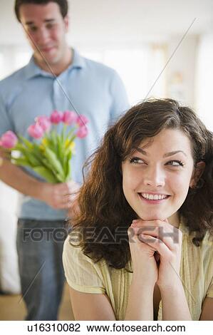 Stock Image - Woman smiling, man with flowers in background. Fotosearch