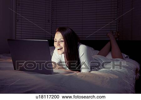 Stock Image - Woman using laptop in bed. Fotosearch