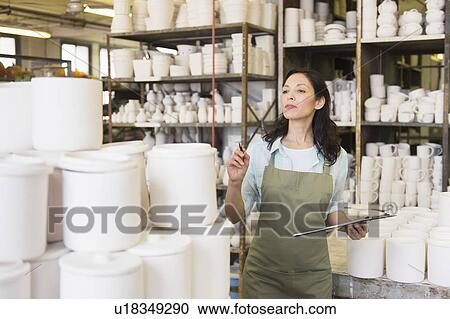 Stock Image - Woman with checklist in pottery warehouse. Fotosearch