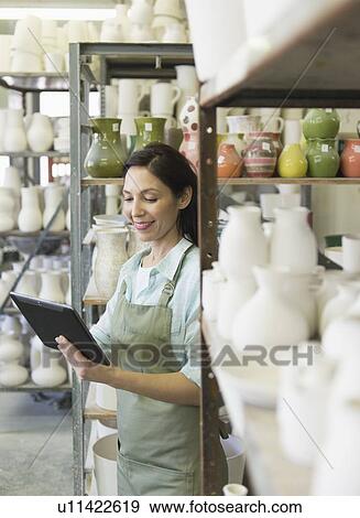 Stock Photo - Woman with digital tablet in pottery warehouse. Fotosearch