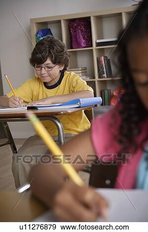 Stock Photo - Writing boy (10-11) with girl (10-11) in foreground. Fotosearch