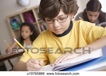 Stock Photograph - Writing boy (10-11) with girls (10-11, 12-13) in background. Fotosearch
