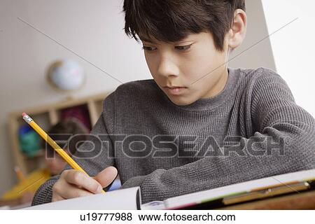 Stock Photo - Writing boy (12-13) with boy (10-11) in background. Fotosearch