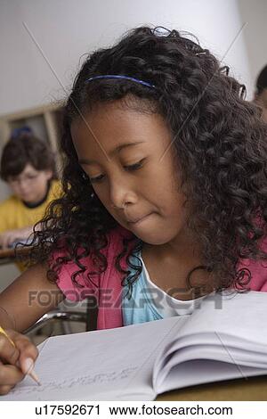 Stock Image - Writing girl (10-11) with boy (10-11) in background. Fotosearch