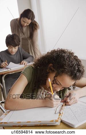 Picture - Writing girl (10-11) with boy (12-13) and teacher in background. Fotosearch