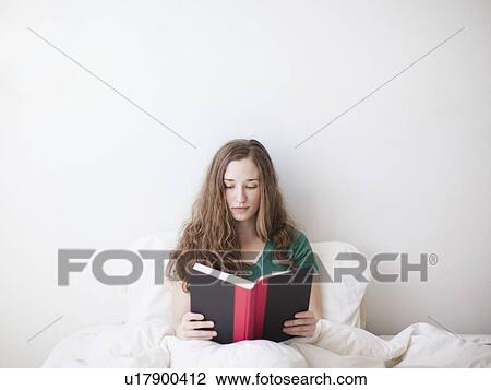 Stock Image - Young attractive woman reading in bed. Fotosearch