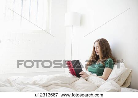 Stock Photo - Young attractive woman reading in bed. Fotosearch