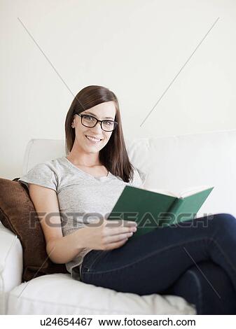 Stock Photo - Young attractive woman sitting on sofa, reading. Fotosearch