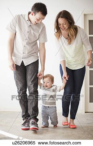 Stock Photography - Young couple assisting baby boy (6-11 months) in first steps. Fotosearch