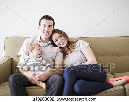 Young couple with baby boy (6-11 months) sitting on sofa View Large Photo Image Stock Image - Young couple with baby boy (6-11 months) sitting on sofa. Fotosearch