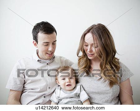 Young couple with baby boy (6-11 months) sitting on sofa View Large Photo Image Stock Image - Young couple with baby boy (6-11 months) sitting on sofa. Fotosearch