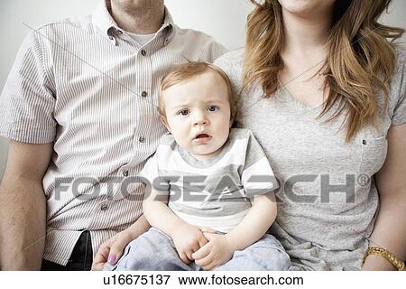 Stock Photo - Young couple with baby boy (6-11 months) sitting on sofa. Fotosearch
