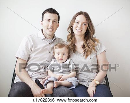 Stock Photograph - Young couple with baby boy (6-11 months) sitting on sofa. Fotosearch