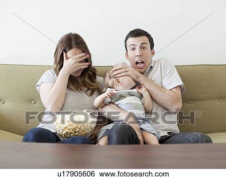 Stock Photograph - Young couple with baby boy (6-11 months) watching horror film . Fotosearch