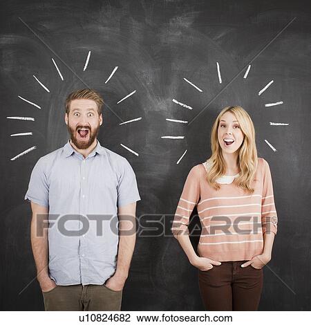 Stock Image - Young couple with blackboard in background, studio shot. Fotosearch