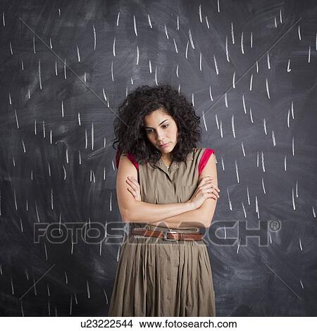 Picture - Young depressed teacher posing against blackboard with V marks imitating rain. Fotosearch