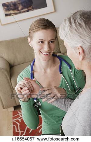Stock Photo - Young female nurse taking pulse of senior woman. Fotosearch