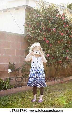 Stock Image - Young girl (4-5) using photographic camera. Fotosearch