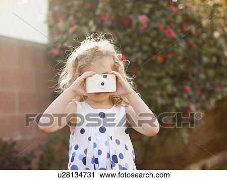 Stock Image - Young girl (4-5) using photographic camera. Fotosearch