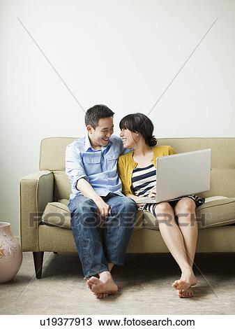 Stock Image - Young happy couple sitting on sofa. Fotosearch