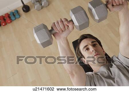 Stock Image - Young man exercising with dumbbell. Fotosearch