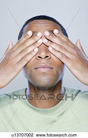 Stock Image - Young man with hands covering eyes, studio shot. Fotosearch