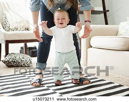 Young mother assisting baby boy (6-11 months) in his first steps View Large Photo Image Stock Image - Young mother assisting baby boy (6-11 months) in his first steps. Fotosearch