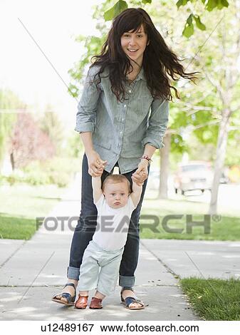Young mother assisting baby boy (6-11 months) in his first steps View Large Photo Image Stock Photo - Young mother assisting baby boy (6-11 months) in his first steps. Fotosearch