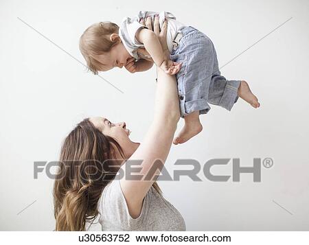 Young mother lifting baby boy (6-11 months) mid-air View Large Photo Image Stock Image - Young mother lifting baby boy (6-11 months) mid-air. Fotosearch