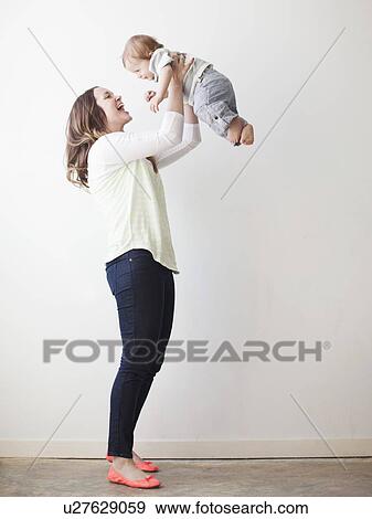 Young mother lifting baby boy (6-11 months) mid-air View Large Photo Image Stock Photo - Young mother lifting baby boy (6-11 months) mid-air. Fotosearch