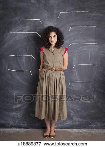 Stock Photo - Young teacher posing against blackboard with blank lines written in chalk. Fotosearch