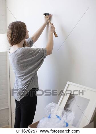 Young woman hanging picture on freshly painted wall View Large Photo Image Stock Photo - Young woman hanging picture on freshly painted wall. Fotosearch