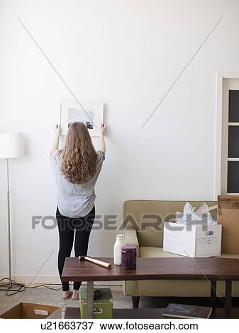 Young woman hanging picture on freshly painted wall View Large Photo Image Stock Photo - Young woman hanging picture on freshly painted wall. Fotosearch
