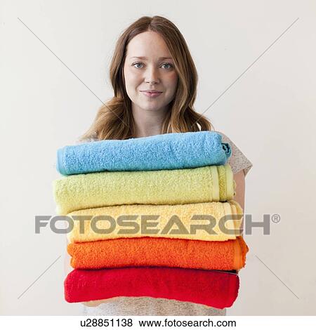 Stock Photo - Young woman holding stack of multi-coloured towels. Fotosearch