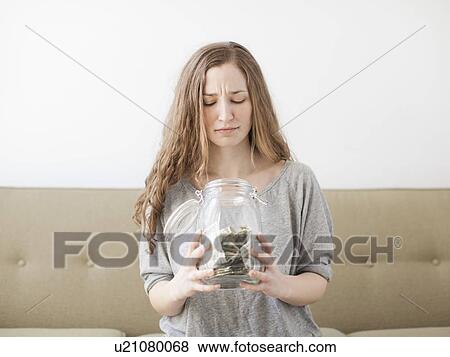 Young woman looking into savings jar with unhappy face expression View Large Photo Image Stock Photo - Young woman looking into savings jar with unhappy face expression . Fotosearch