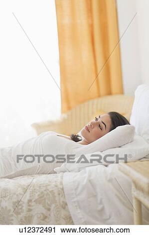 Stock Image - Young woman lying on bed. Fotosearch