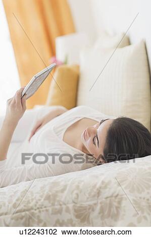 Young woman lying on bed using tablet pc View Large Photo Image Stock Image - Young woman lying on bed using tablet pc. Fotosearch