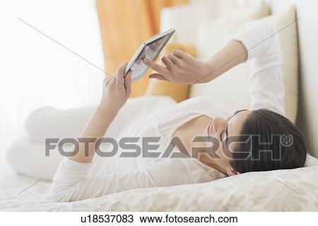 Young woman lying on bed using tablet pc View Large Photo Image Stock Image - Young woman lying on bed using tablet pc. Fotosearch