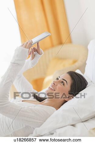 Young woman lying on bed using tablet pc View Large Photo Image Stock Photo - Young woman lying on bed using tablet pc. Fotosearch