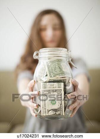 Stock Image - Young woman presenting her savings jar . Fotosearch