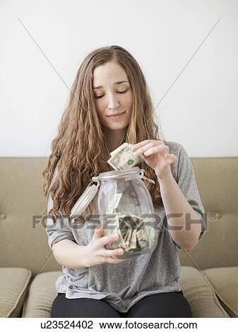 Young woman putting money into her savings jar View Large Photo Image Stock Image - Young woman putting money into her savings jar . Fotosearch